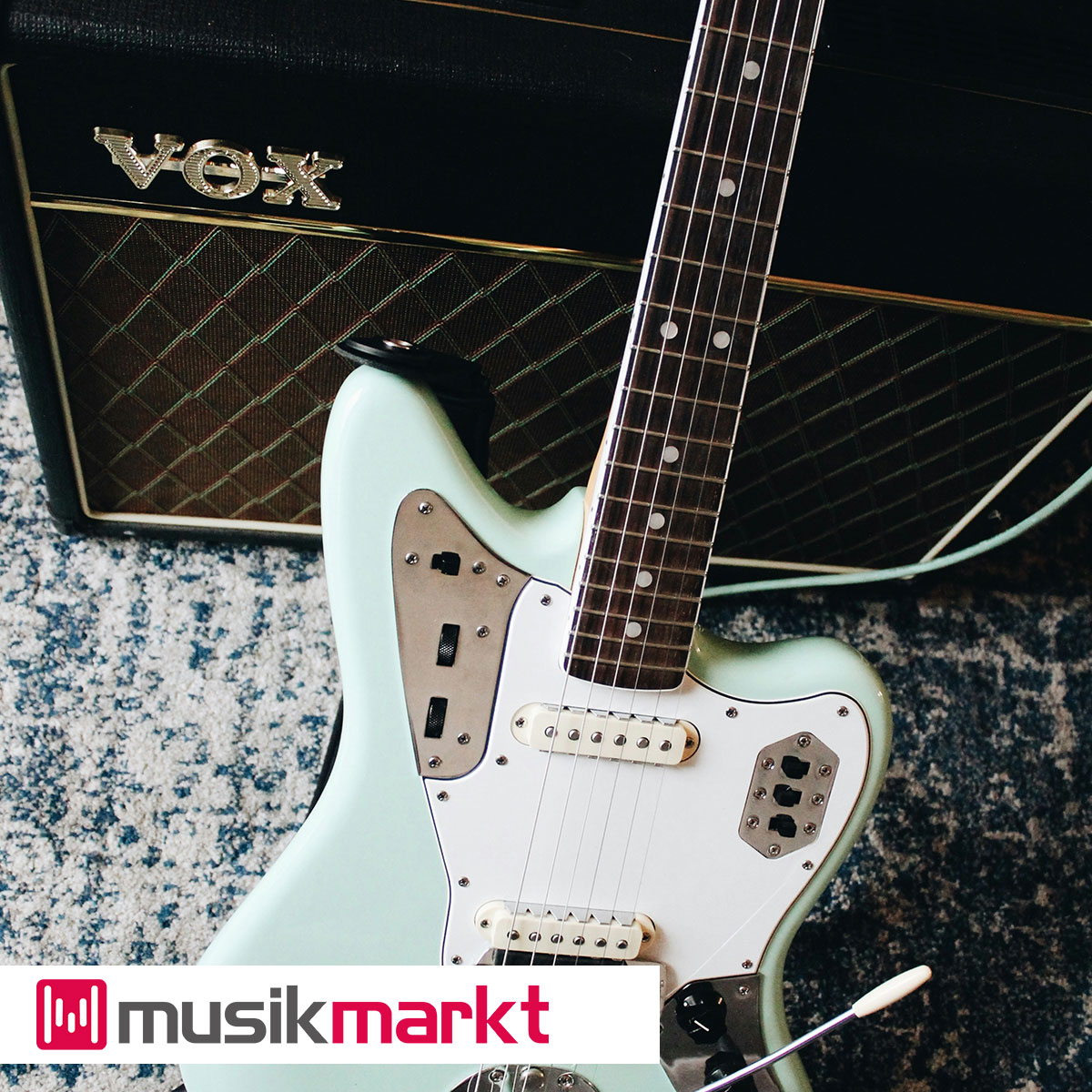 Schwarzer VOX Verstärker mit einem Goldenen Logo. Davor steht eine mint-weiße E-Gitarre.